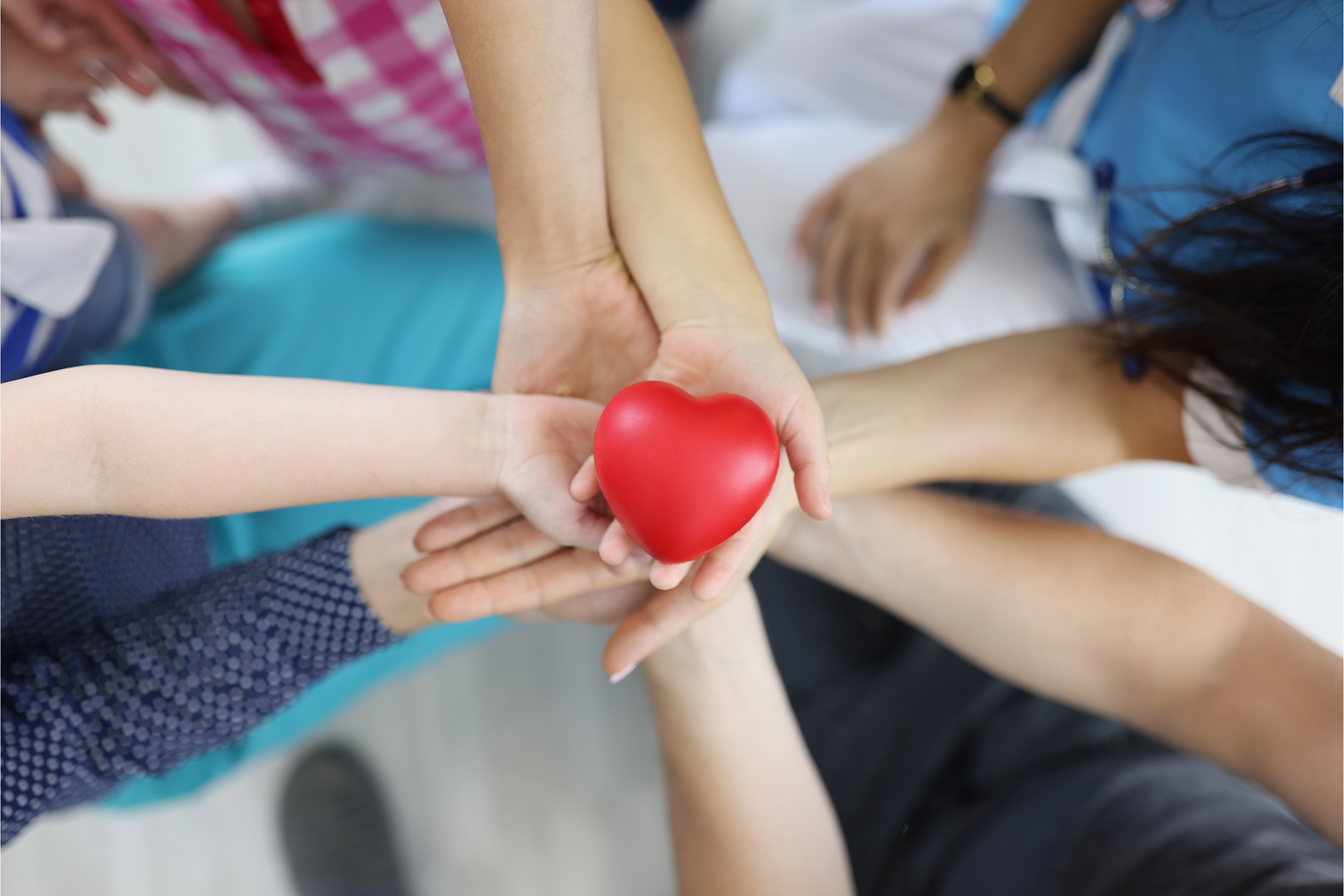 A birds-eye view of a circle of hands holding a red heart, representing the charity supporter journey