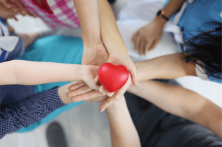 A birds-eye view of a circle of hands holding a red heart, representing the charity supporter journey-1