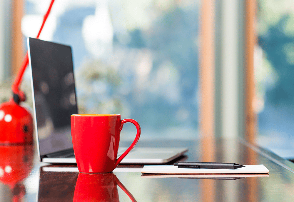 A laptop, pen and paper and red mug on a desk, representing data audits as part of how to generate income for a charity.