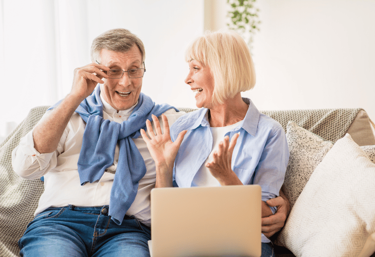 A senior couple celebrating a lottery or raffle win on their laptop, representing income generation strategy ideas for charity organisations.