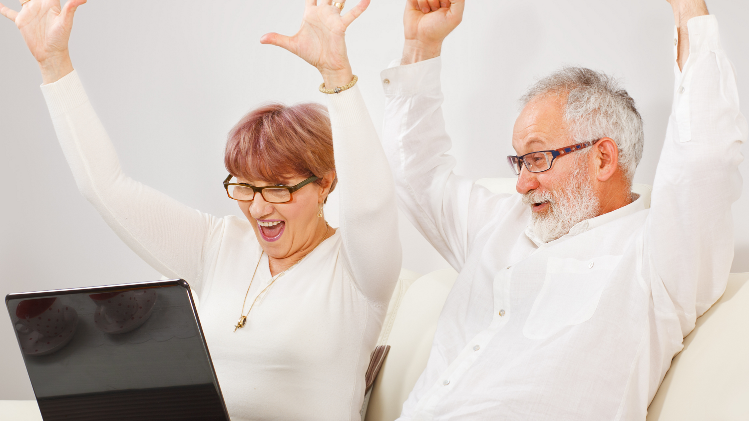A senior couple cheering after winning the lottery on their laptop, representing the impact of using a charity lottery service