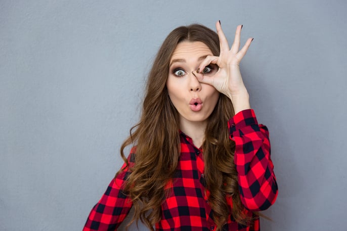 Funny amusing curly girl in checkered shirt showing okay gesture near her eye