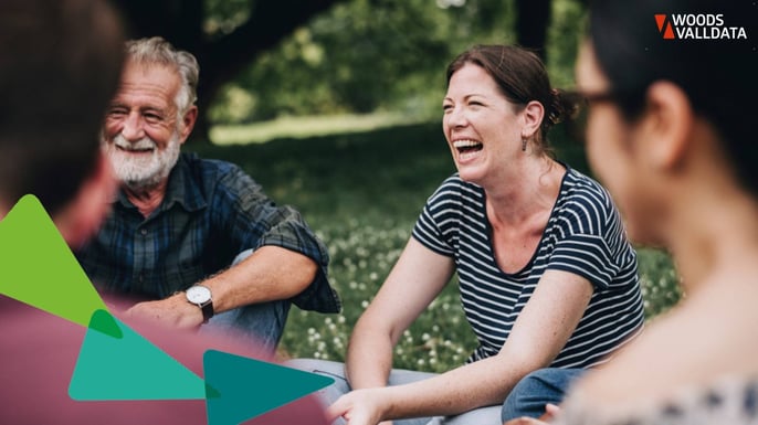 circle of middle aged people sat in park in a circle laughing WV Brand