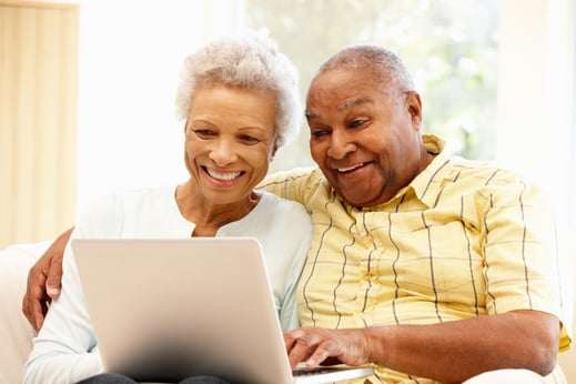 old white heared couple sitting close together on a sofa looking at a lap top and smiling