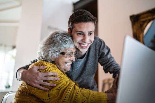 older lady and young man hugging facing a laptop screen and smiling with joy